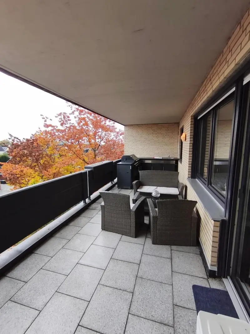 Überdachter Balkon mit Loungeecke und Blick in die Baumkronen